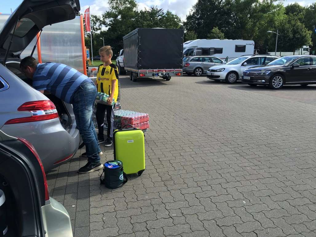 Far og sønn ved bilen på parkeringsplass. De pakker bilen med varer de har kjøpt på kjøpesenter.
