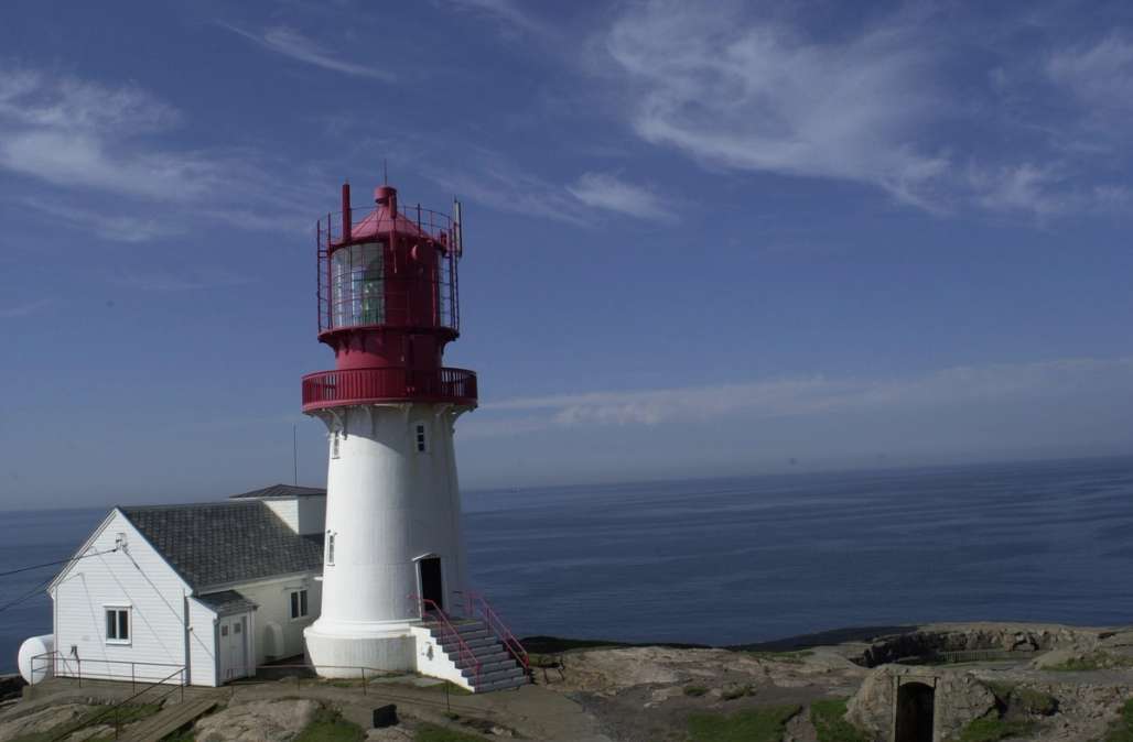 a red and white lighthouse on top of a cliff overlooking the ocean .