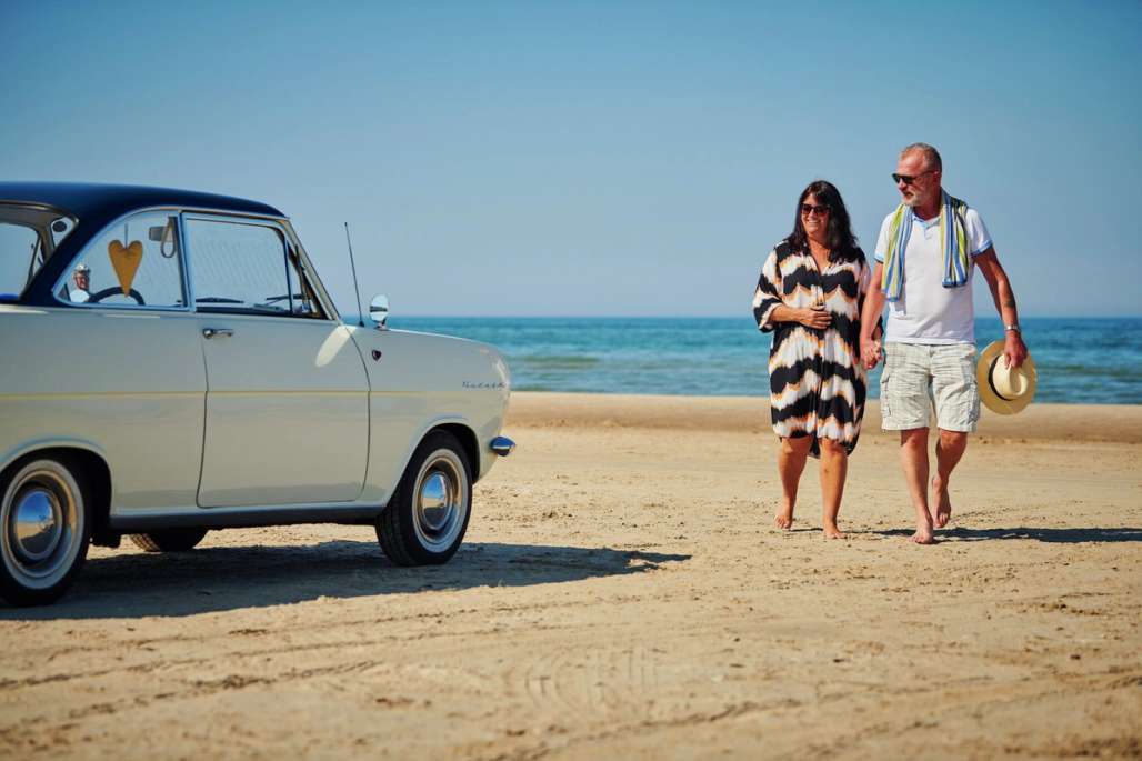 Par og bil på stranden. Foto. 