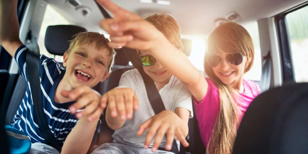 Three children having fun in the back seat of a car.