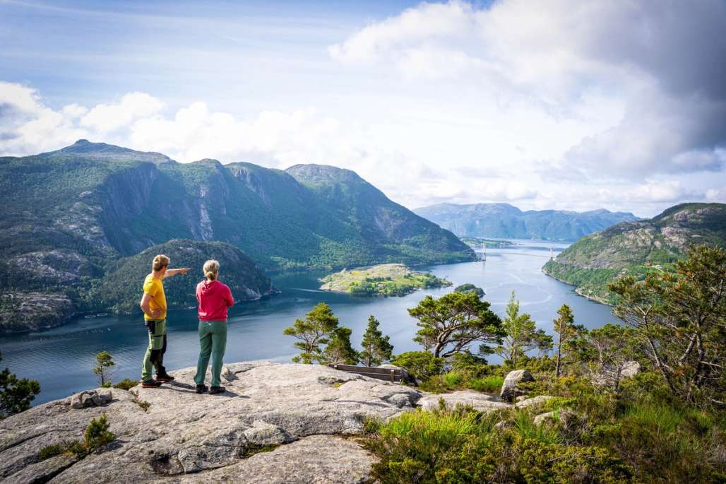 Two people standing on a mountain, looking out over the fjord and mountain landscape.