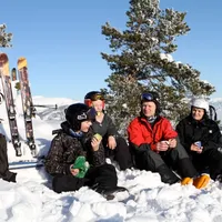 Eine Skifahrerfamilie macht eine Pause im Schnee und genießt Snacks unter klarem blauen Himmel.
