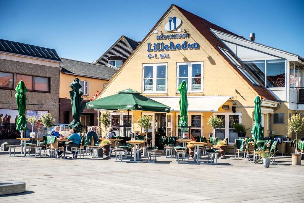 Uteservering ved Restaurant Lilleheden med grønne parasoller og gjester som nyter mat og drikke under en klar blå himmel.