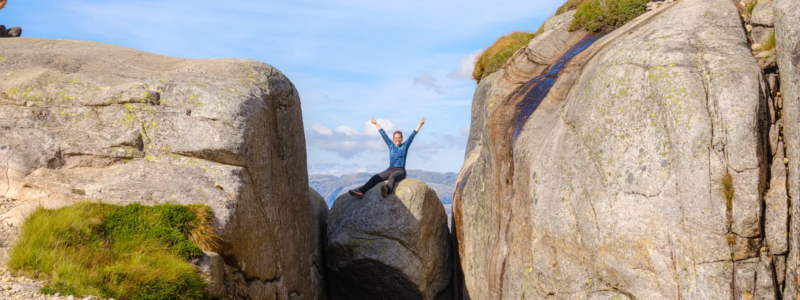 Man sits with his hands in the air on Kjeragbolten.