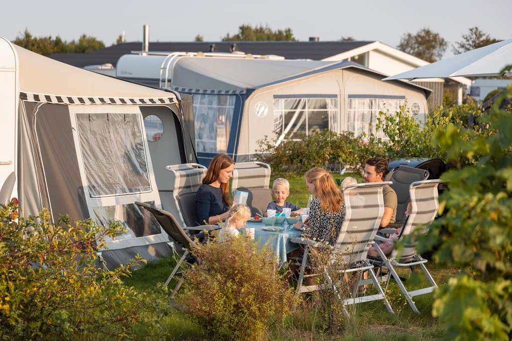 Familie sitter rundt et bord og spiser på campingplass.