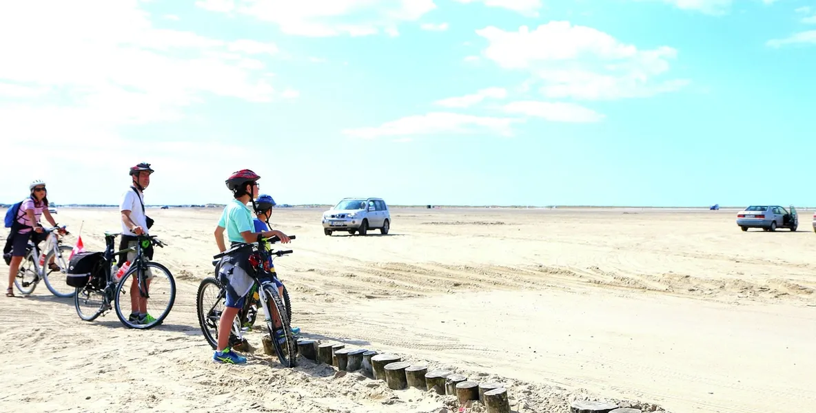 Langsstrakt strand med sykler, biler og folk