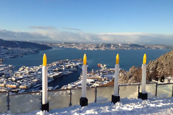 Vier große Kerzen mit Blick auf eine verschneite Stadtlandschaft von Bergen im Winter.
