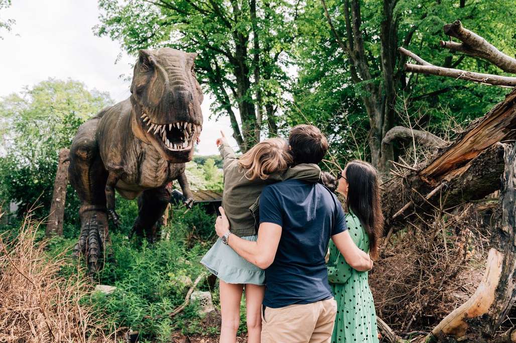 Familie står inne i skogen og ser på en dinosaur i naturlig størrelse.