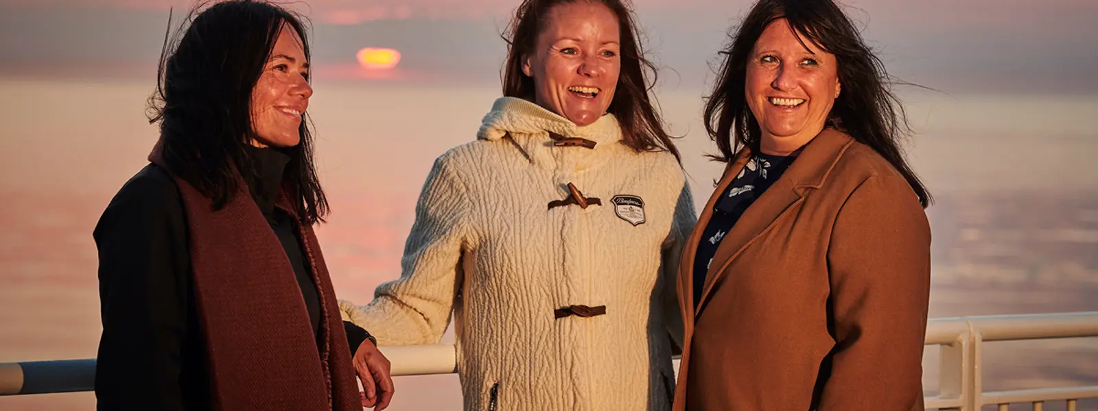 Tre damer hygger seg på deg i solnedgangen.