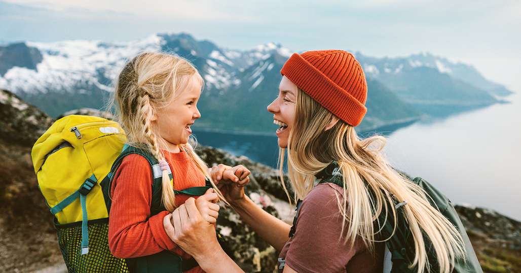 Smiling lady and girl at the top of a mountain.