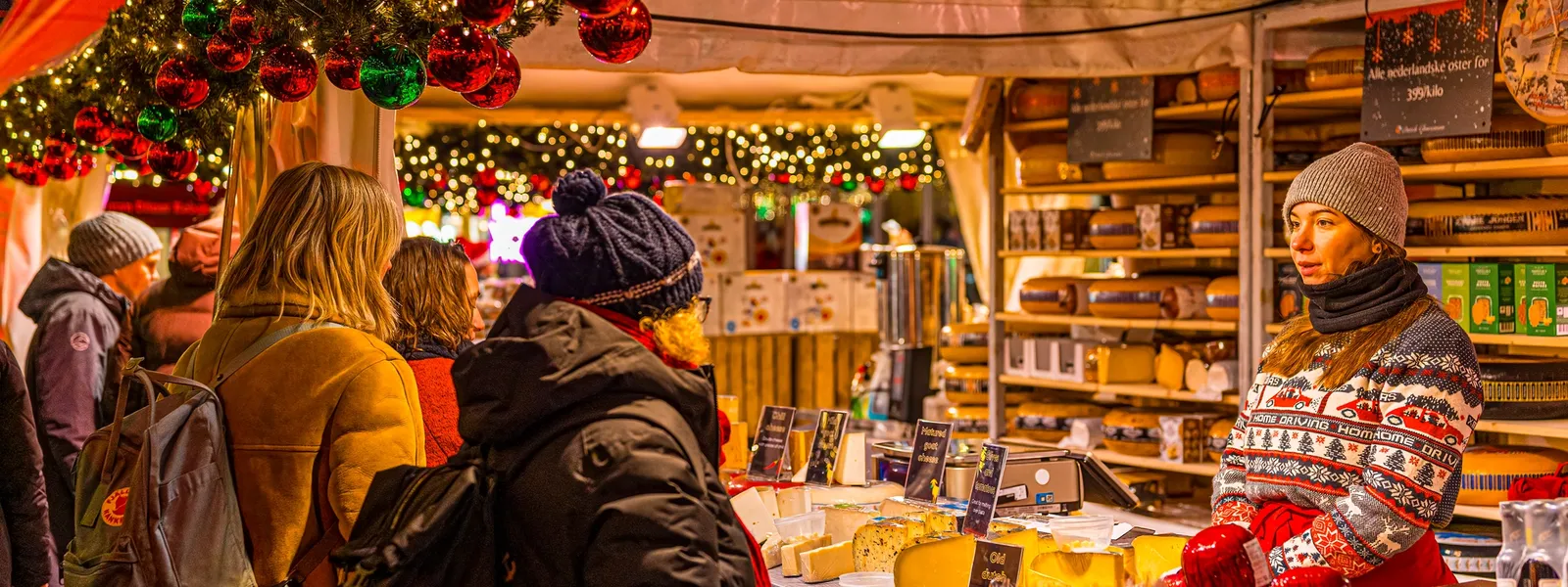A couple holds hands and smiles while walking down a decorated street during the Christmas season.