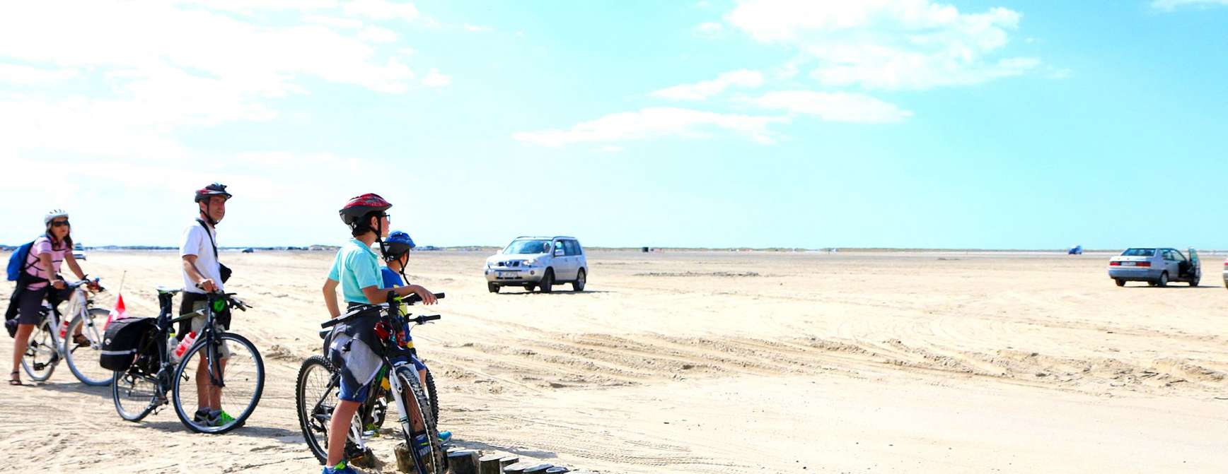 Langsstrakt strand med sykler, biler og folk