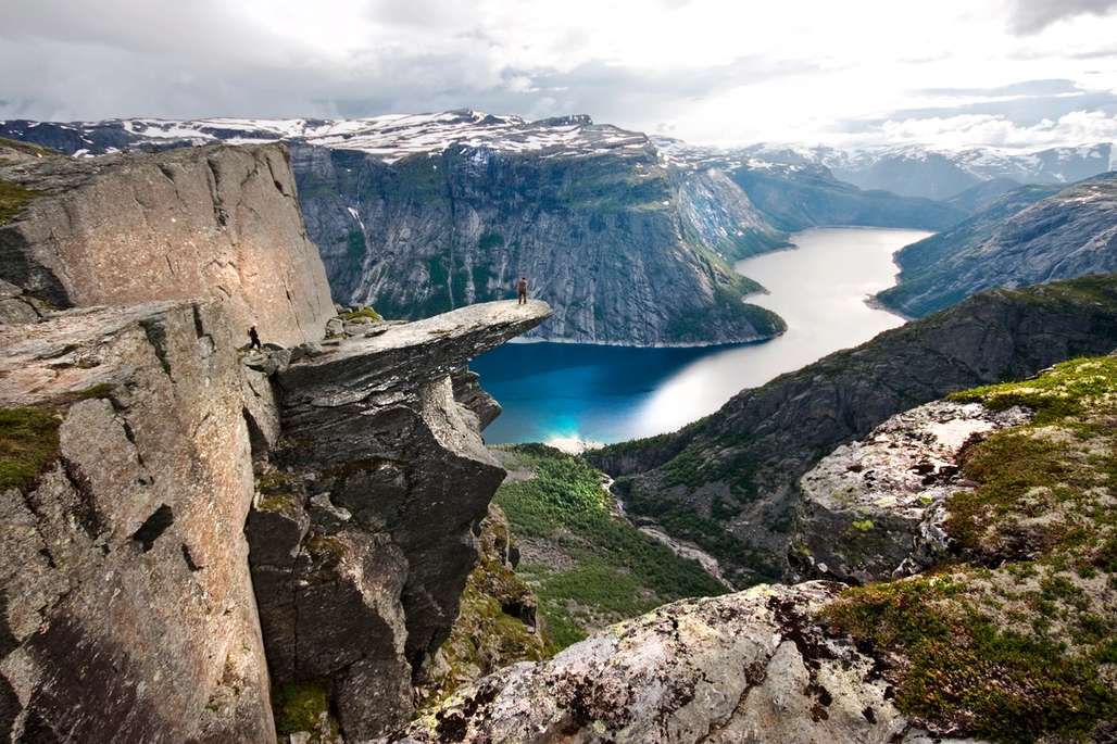 Person standing on Trolltunga surrounded by fjords and mountains.