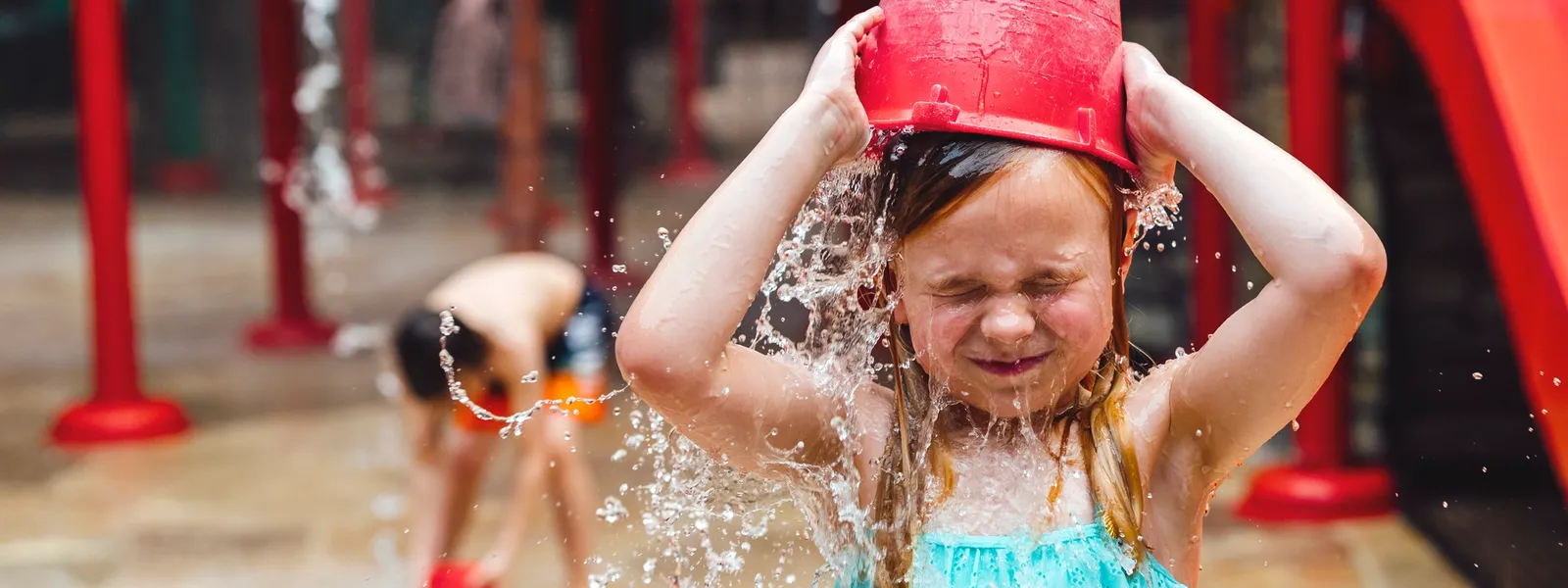 Jente i badeland som tømmer vann over hodet med rød bøtte.