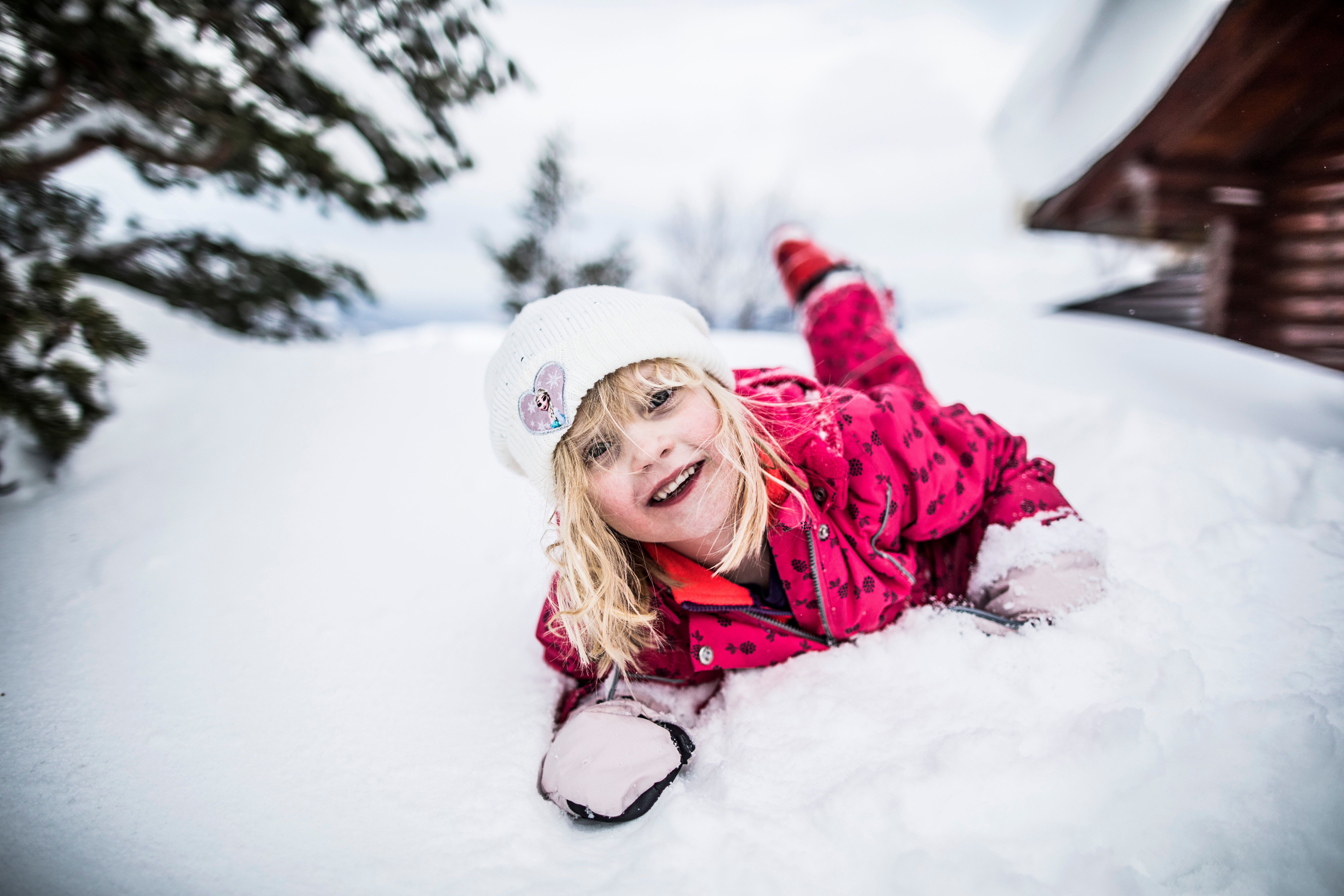 a little girl is laying on her stomach in the snow .