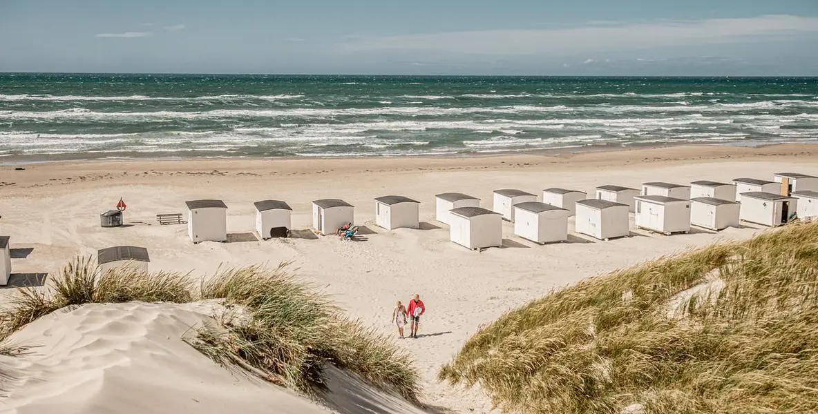 Strand med badehus og et par som vandrer bort fra stranden.