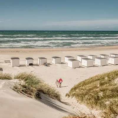 Strand med badehus og et par som vandrer bort fra stranden.