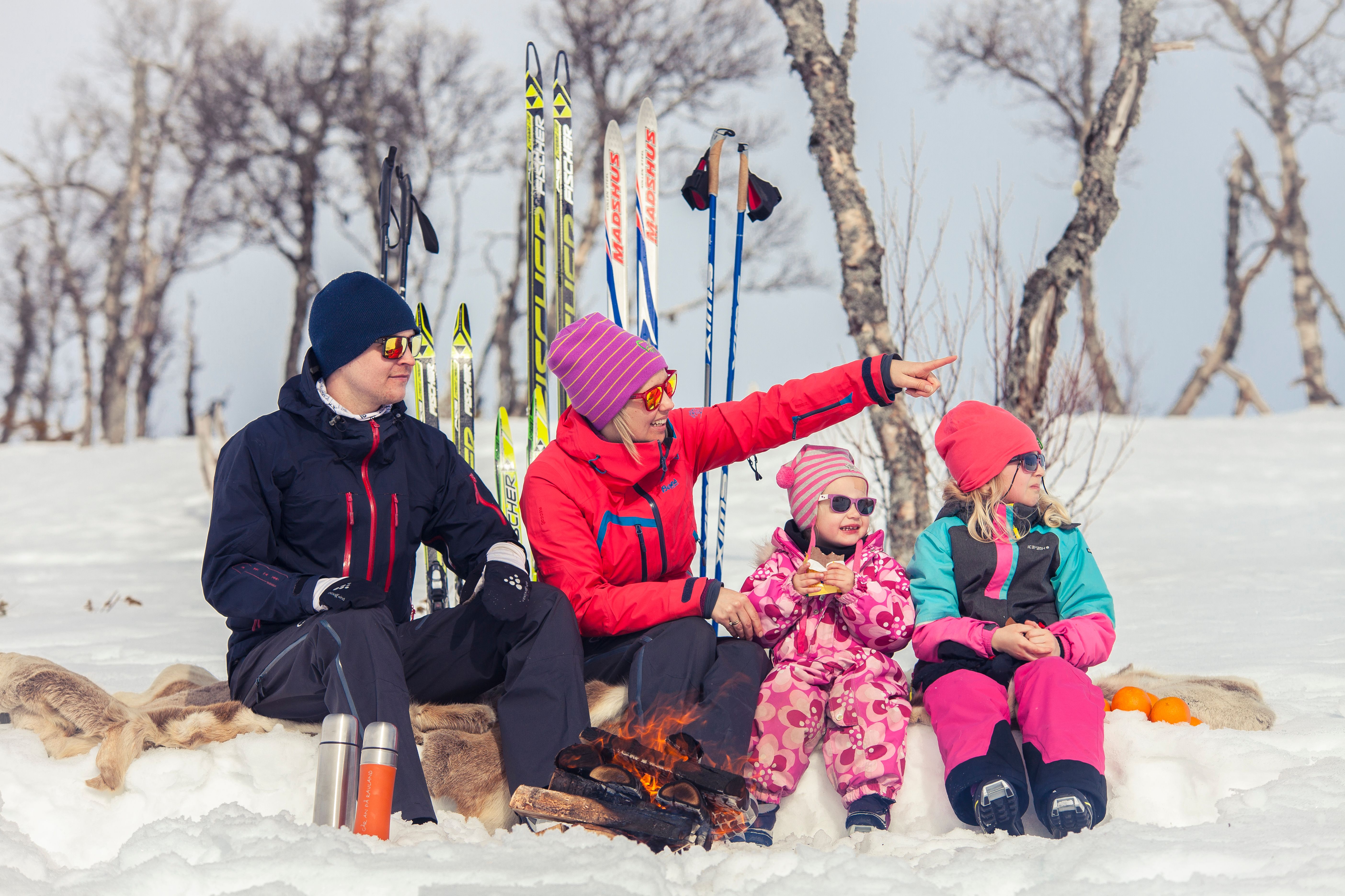 a family is sitting around a fire in the snow .