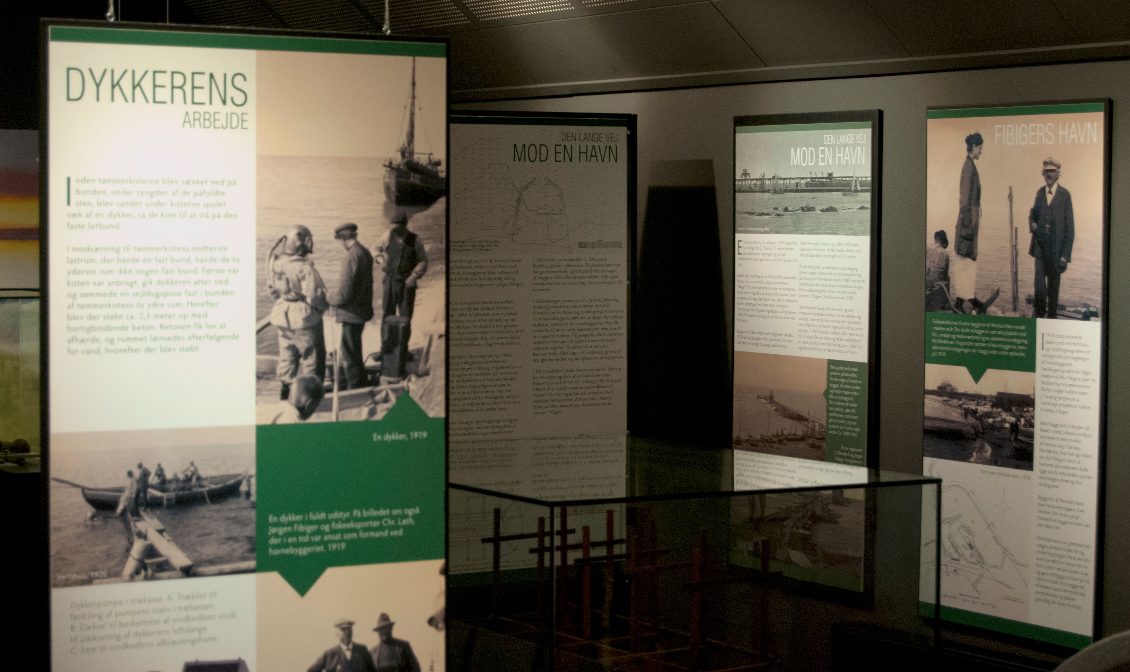 En museumsutstilling som viser informasjonstavler om dykkerarbeid og havnehistorie, inkludert bilder av dykkere og historiske havneanlegg.