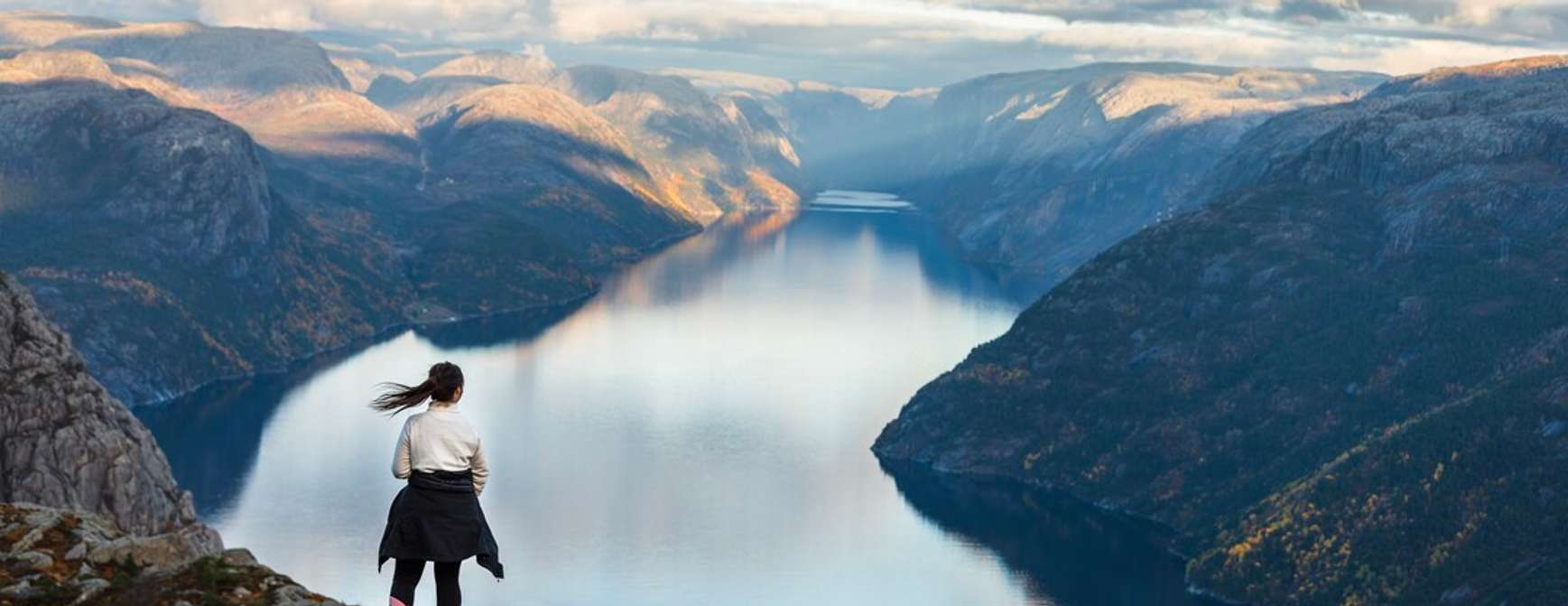 Eine Frau steht auf einem Berg und schaut über einen Fjord.