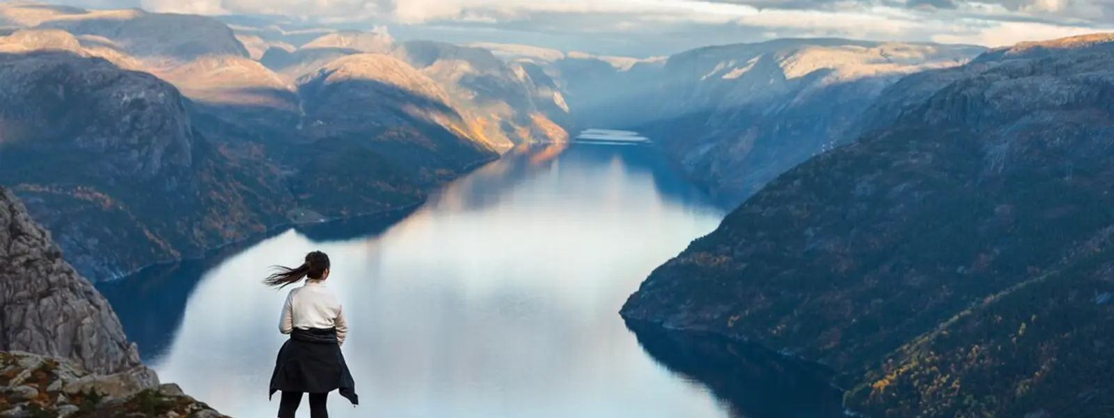 Dame står på et bjerg og ser ud over en fjord.