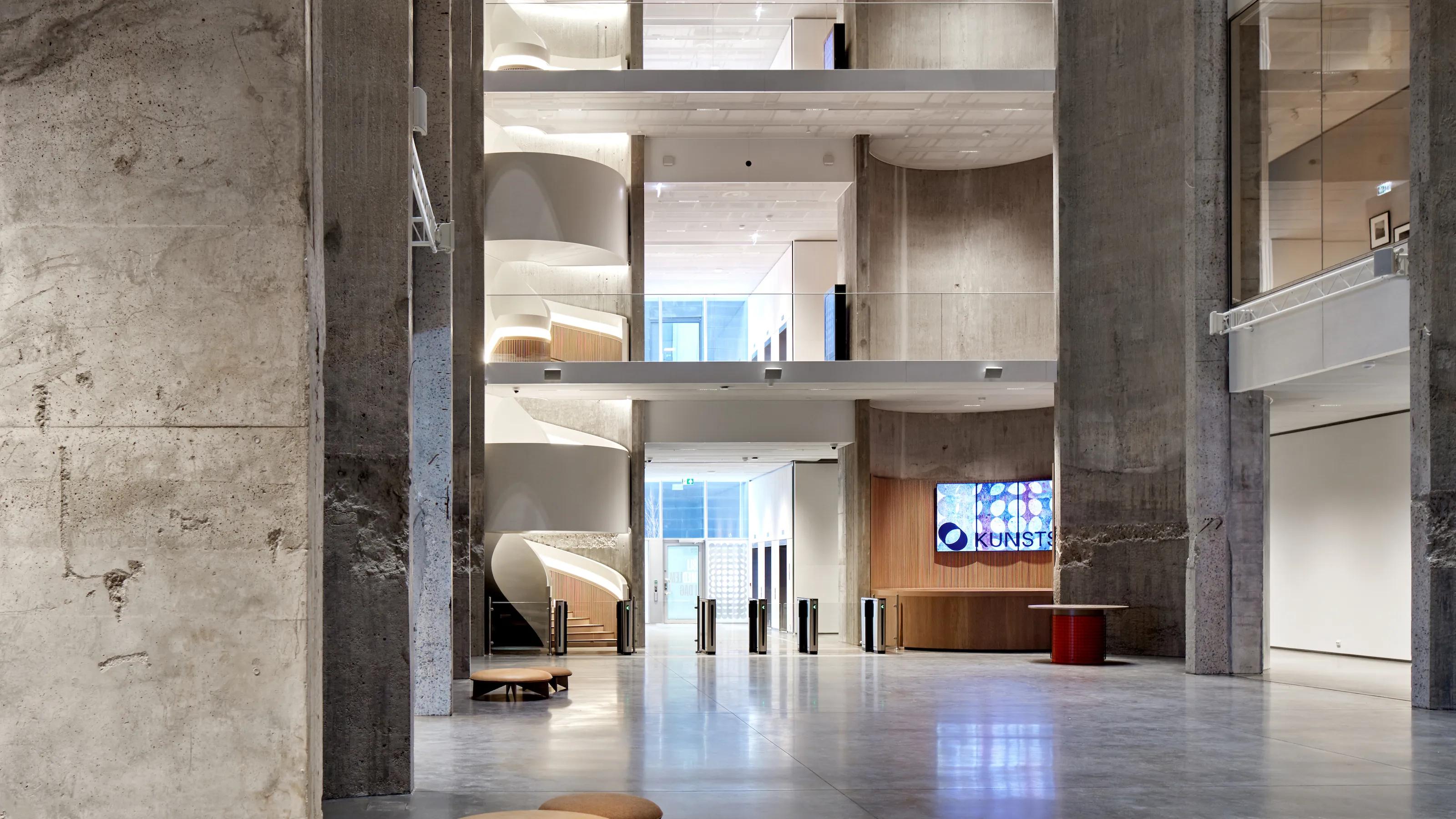 Interior image of a modern building with concrete walls and multiple floors showing staircases and a reception area.