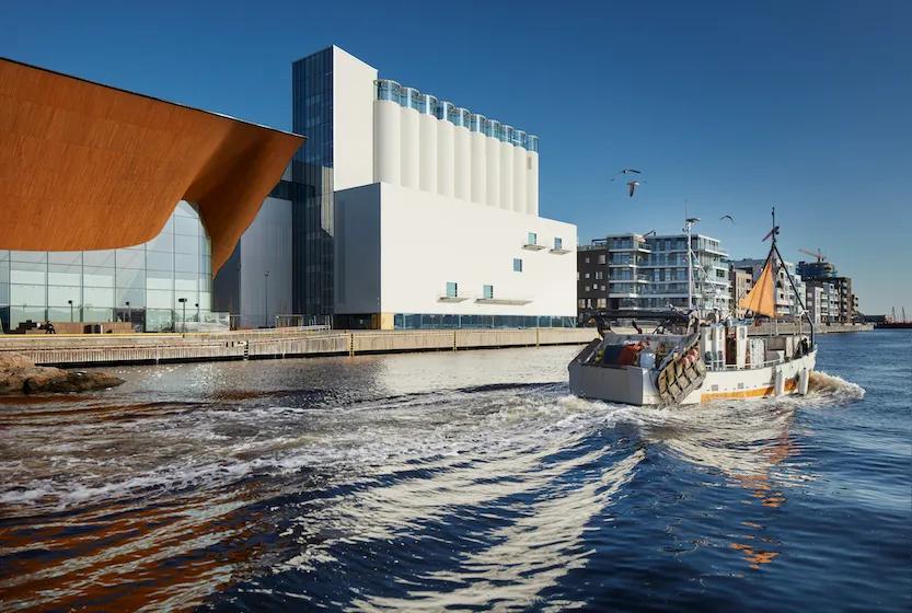 A boat sailing on a canal with modern buildings in the background under a clear blue sky.