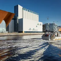 Ein Boot fährt auf einem Kanal mit modernen Gebäuden im Hintergrund unter einem klaren blauen Himmel.