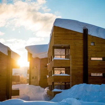 Træhytter med snedækkede tage, badet i gyldent lys fra den nedgående sol.