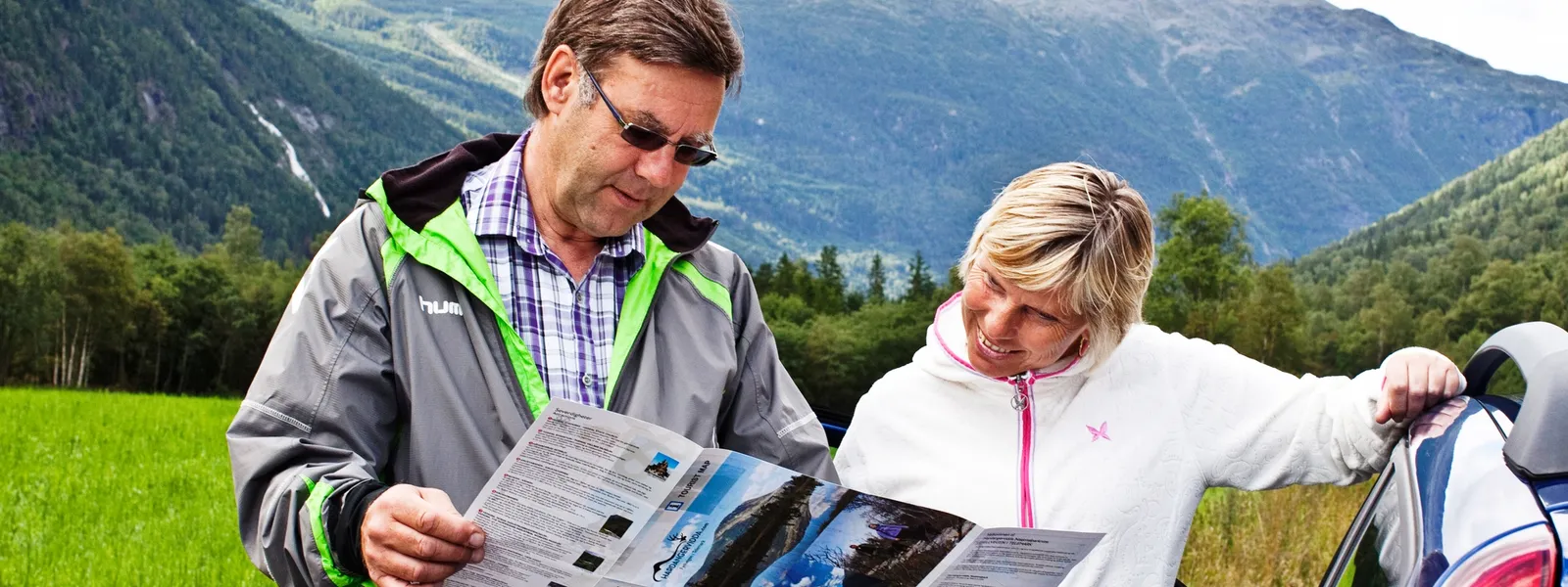 A man and a woman are standing outside in nature, looking at a brochure.