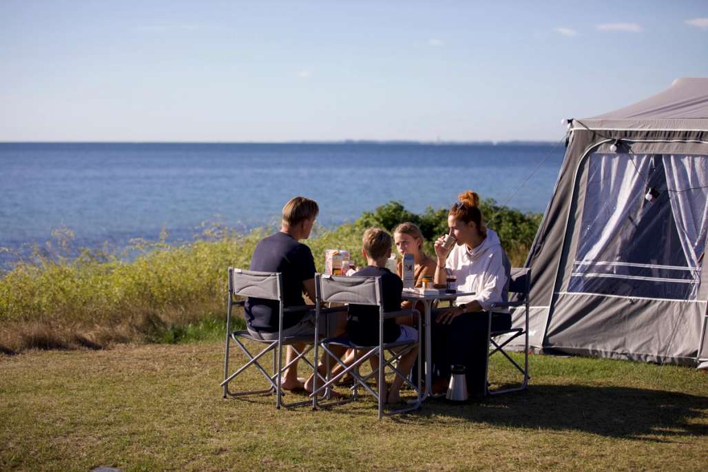Familie på campingferie sitter og spiser frokost utenfor teltet.