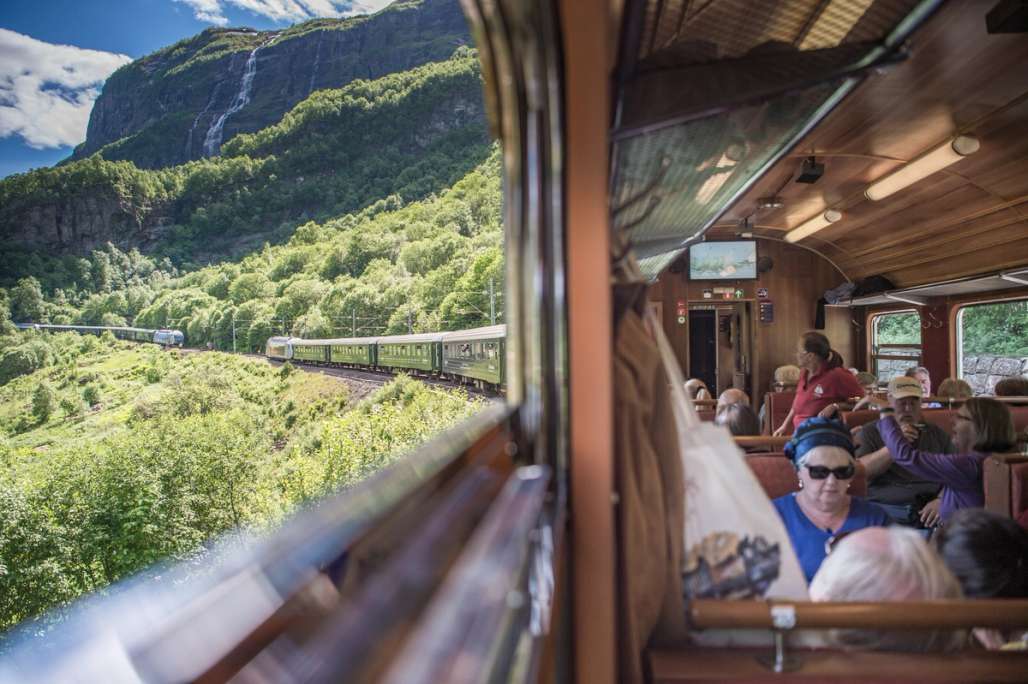 a group of people are sitting on a train looking out the window at a mountain .