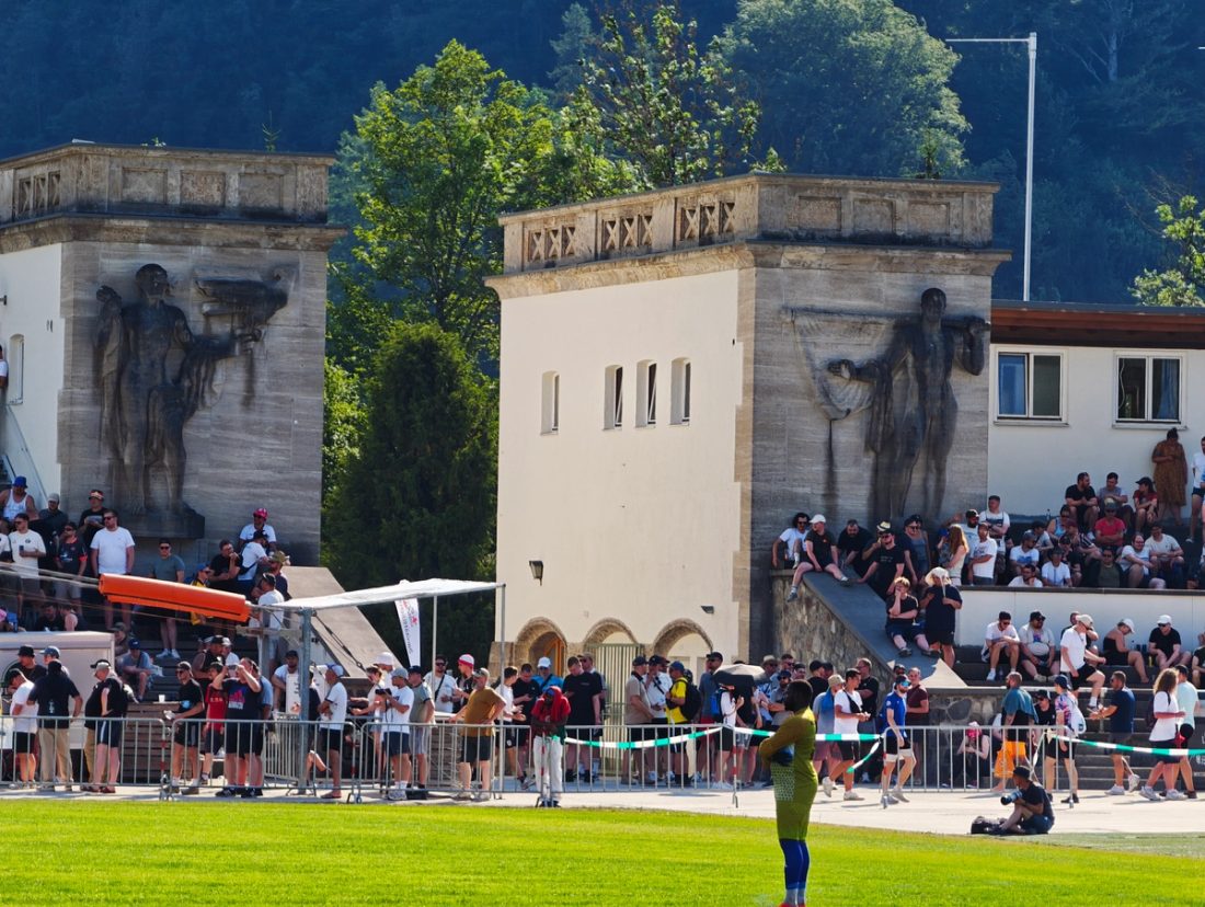 Zuschauer vor den markanten alten Gebäuden und Tribünen des Olympiastadions Garmisch-Partenkirchen während des Fußballspiels.