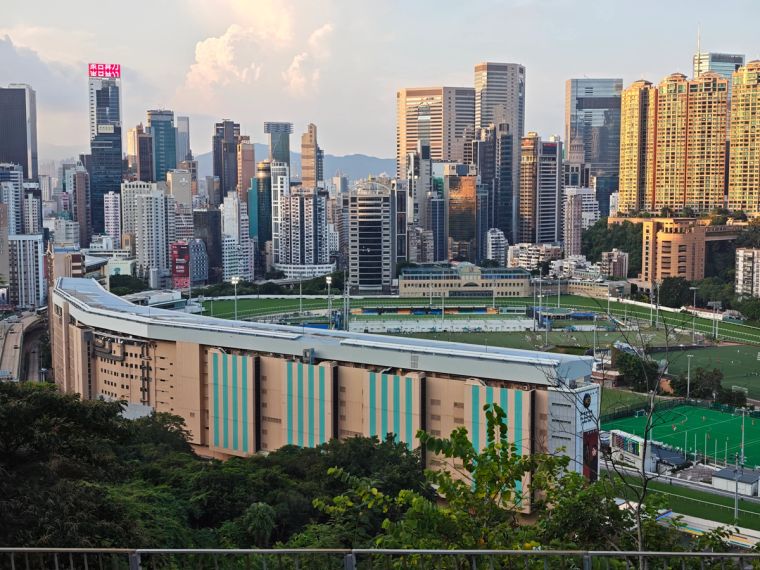 Fußballspiel im Hong Kong Football Club in Happy Valley zwischen Lucky Mile und New Fair Kui Tan FC. Im Hintergrund ragen zahlreiche Wolkenkratzer über den Kunstrasenplatz unter Flutlicht.