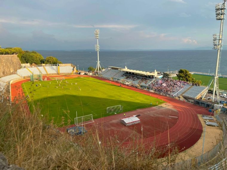 Blick von oben auf das Stadion Kantrida in Rijeka, Kroatien, während eines Fußballspiels. Zu sehen sind das Spielfeld, die Laufbahn, besetzte Tribünen und die Adria direkt hinter dem Stadion.