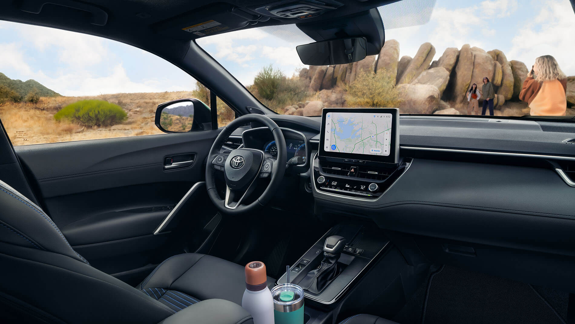 View from inside a toyota Corolla Cross suv showing the steering wheel, dashboard with GPS screen, and two bottles in the cup holders.