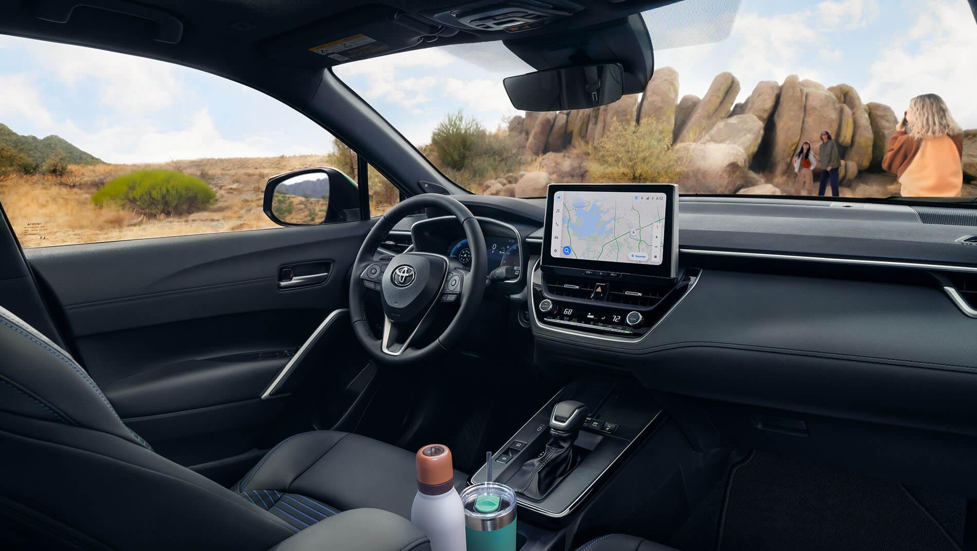View from inside a toyota Corolla Cross suv showing the steering wheel, dashboard with GPS screen, and two bottles in the cup holders.