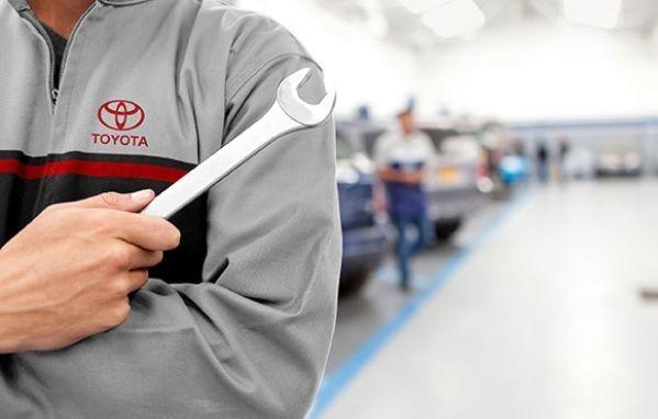 Toyota Genuine Service Professional standing in a Toyota car service bay holding a wrench