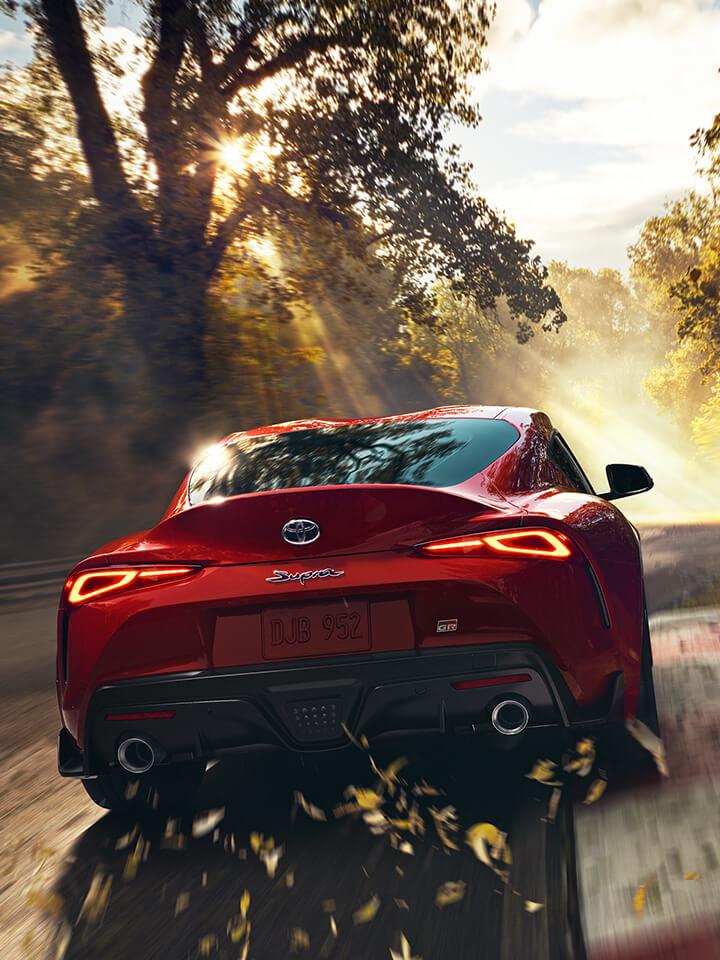 Red Toyota Supra driving down a forest road with light streaming through the trees