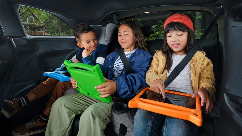 Three children sit in the backseat of a 2025 toyota sienna, each using a colorful tablet.