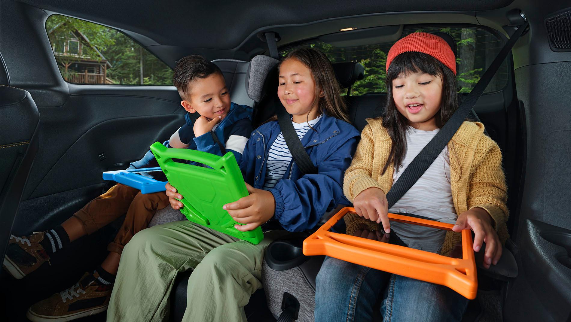 Three children sit in the backseat of a 2025 toyota sienna, each using a colorful tablet.