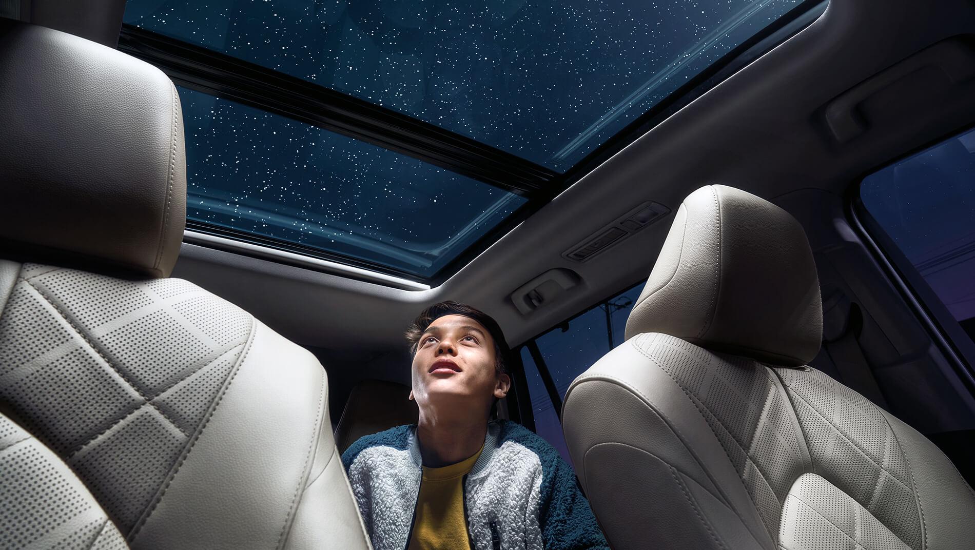 man inside the back seat of a Toyota Highlander looking out of the panoramic moonroof at the stars