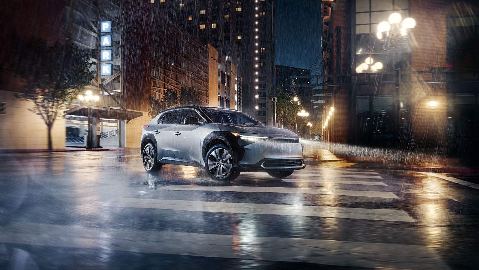 2024 silver Toyota bZ4x all electric plug in vehicle driving in a city parking lot at night in the rain