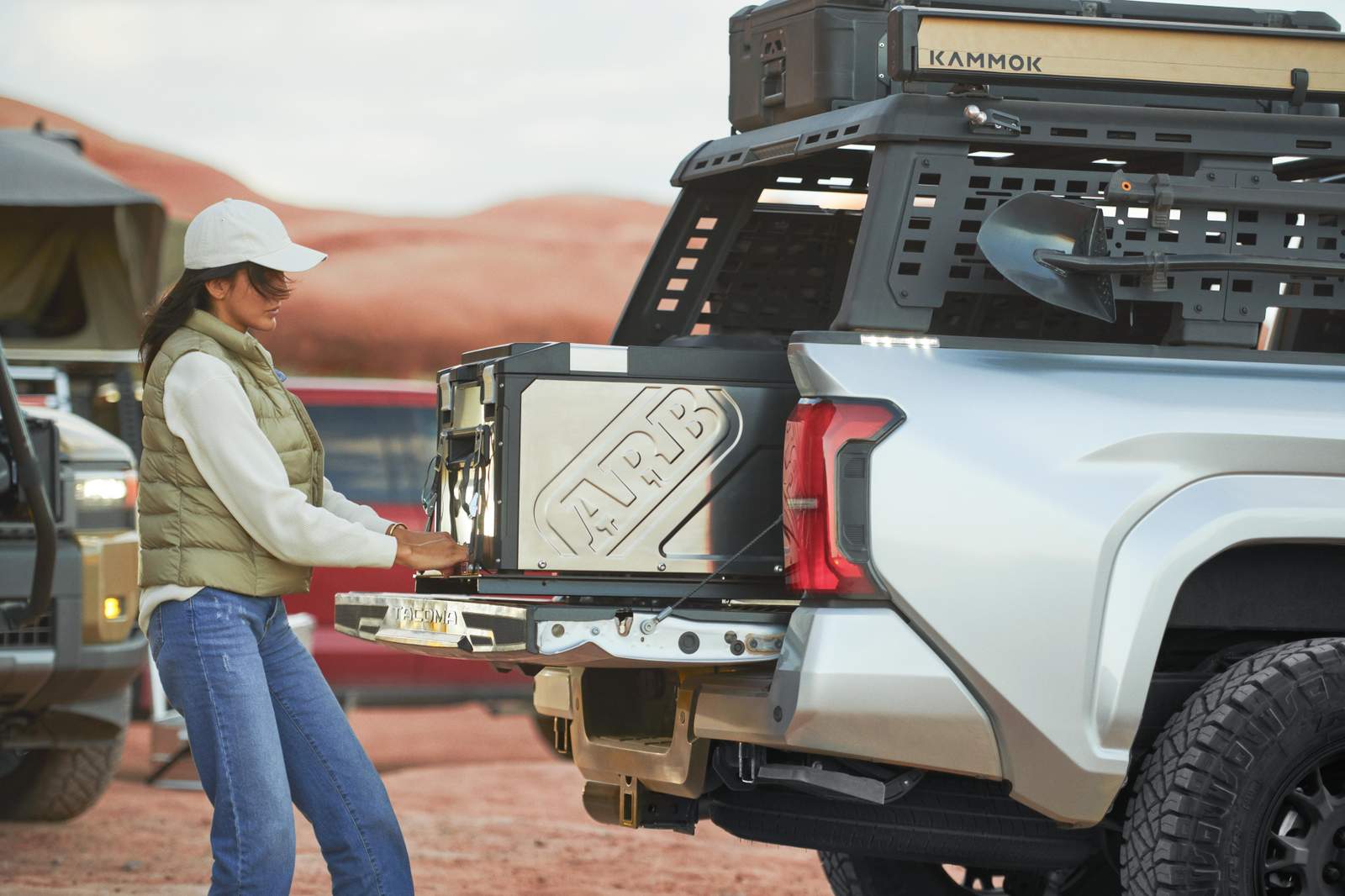 A person opens a drawer from the back of a silver toyota tacoma off-road vehicle equipped with outdoor gear.