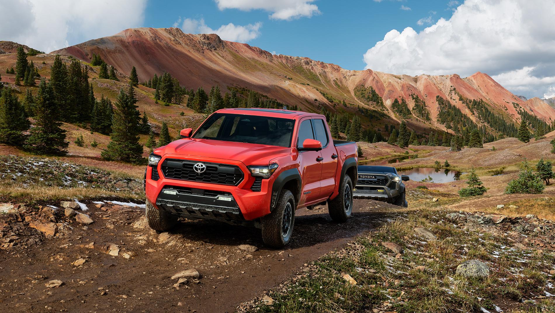 2024 red Toyota Tacoma driving down a dirt road followed by  grey Toyota Tacoma with dirt mountains in the background