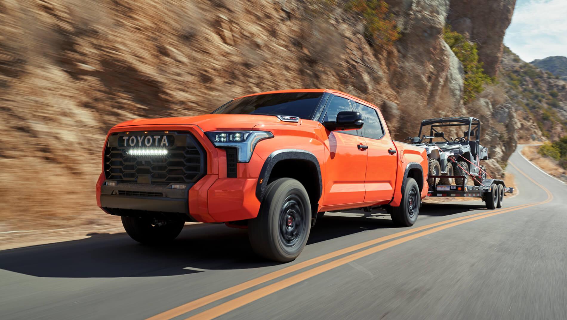Orange Toyota Tundra pulling trailer with toys up a mountain road