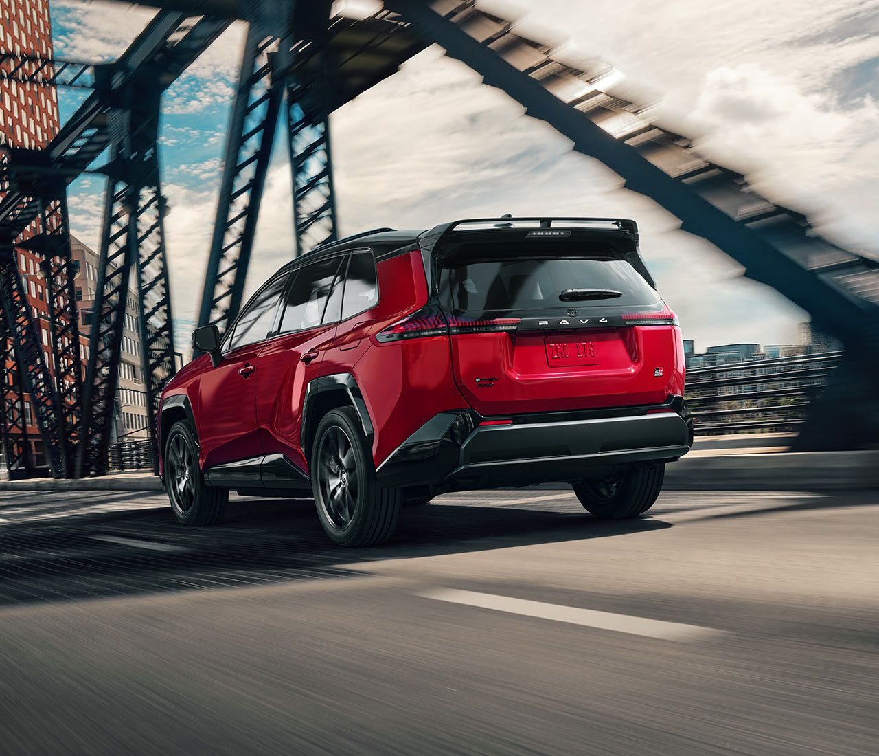 A Toyota RAV4 drives across a bridge in an urban setting, viewed from the rear.