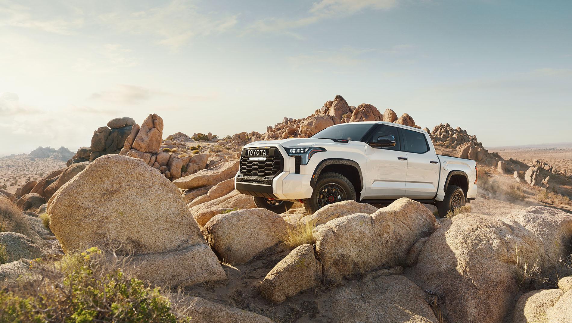 A white 2024 Toyota Tundra parked on rugged rocky terrain in a desert landscape.