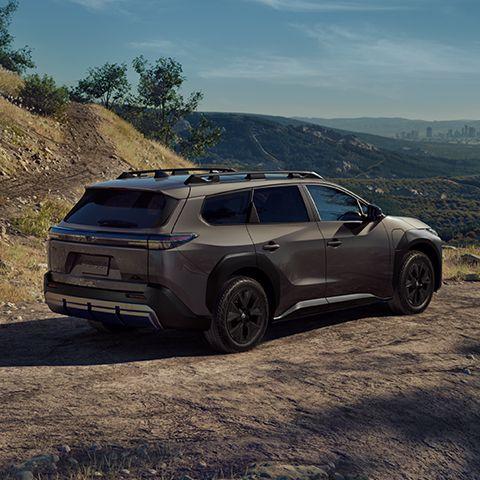 A brown toyota 2026 bzW SUV driving on a dirt road through a hilly landscape.