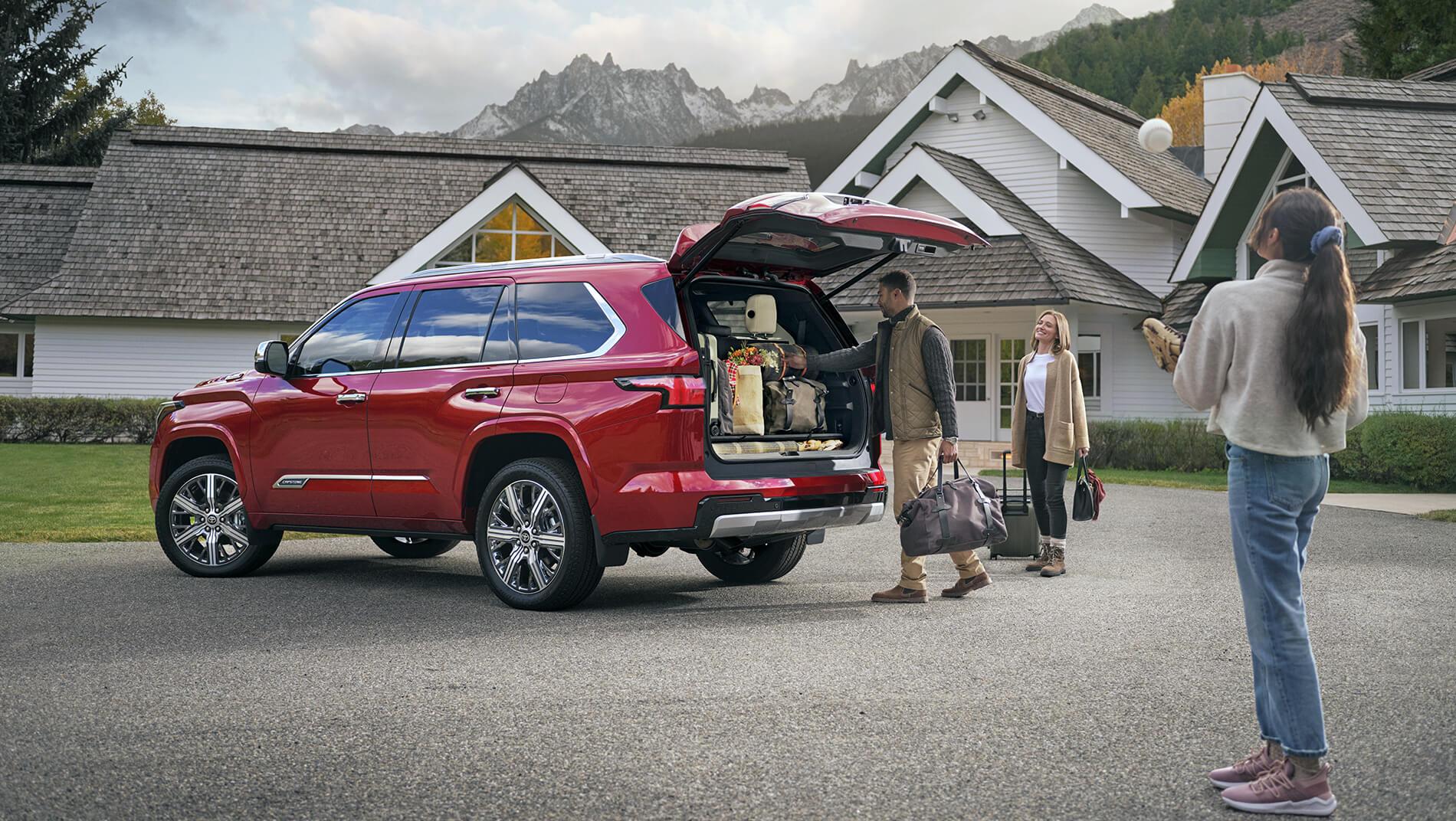 family loading luggage into large cargo space of a red Toyota Sequoia